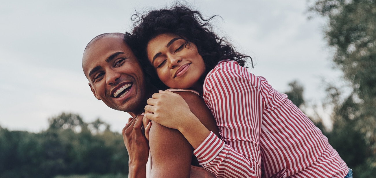 Happy young couple embracing and smiling while sitting outdoors People excited about their affordable dental care with Renovo